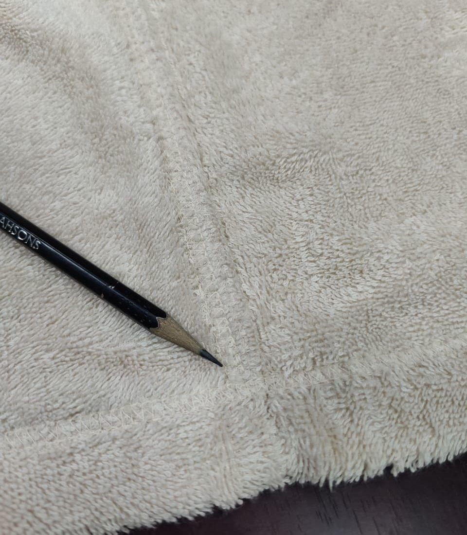 Pencil pointing to the overlocked junction of two seams on a beige terry bathrobe